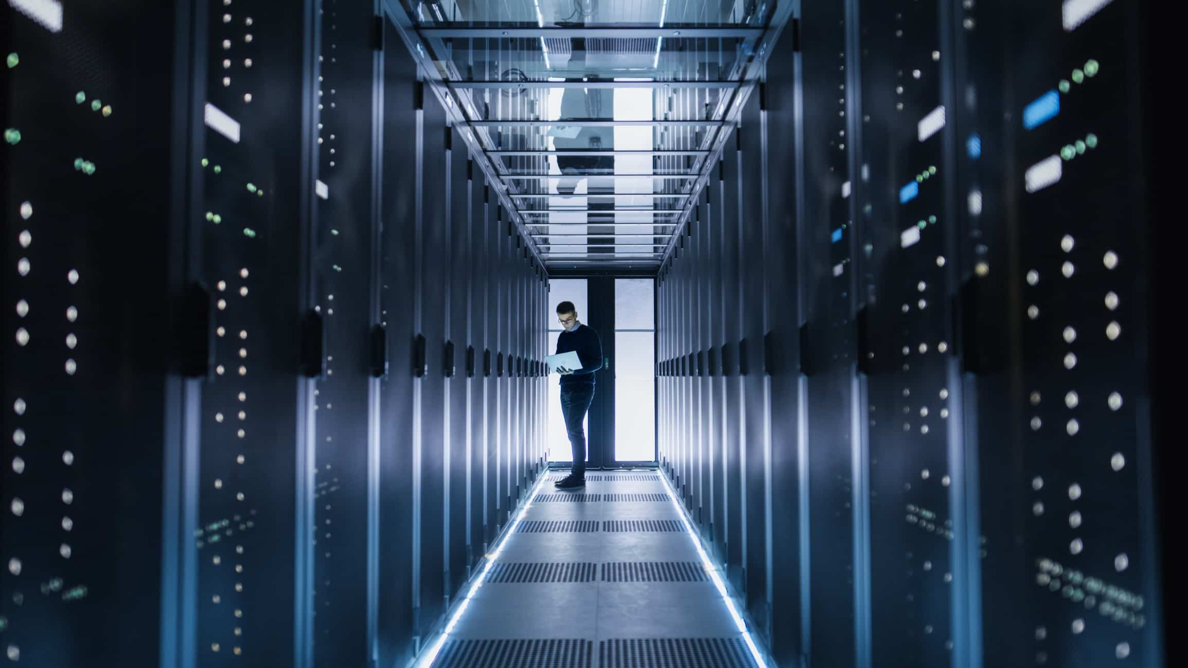 Male IT Engineer Works on a Laptop in a Big Data Center. Rows of Rack Servers are Seen. The Difference Between Data Management vs Data Governance